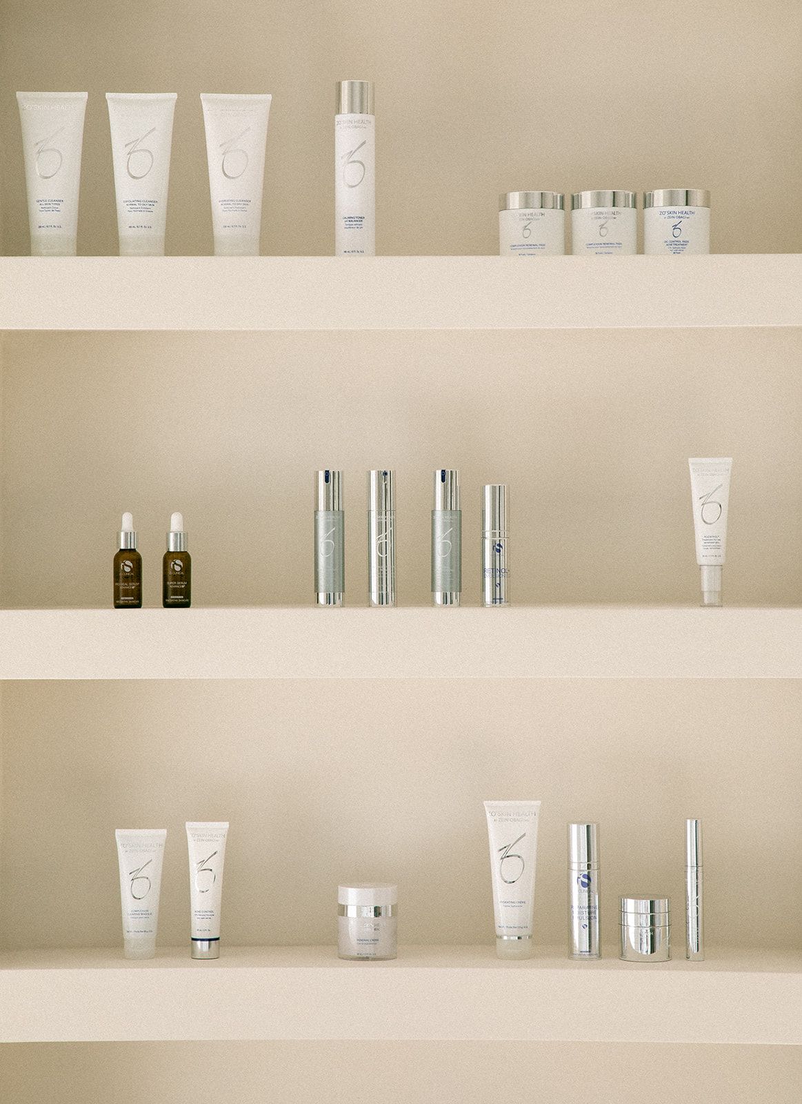 Collection of minimalist skincare products arranged on light beige shelves including tubes, bottles and jars.