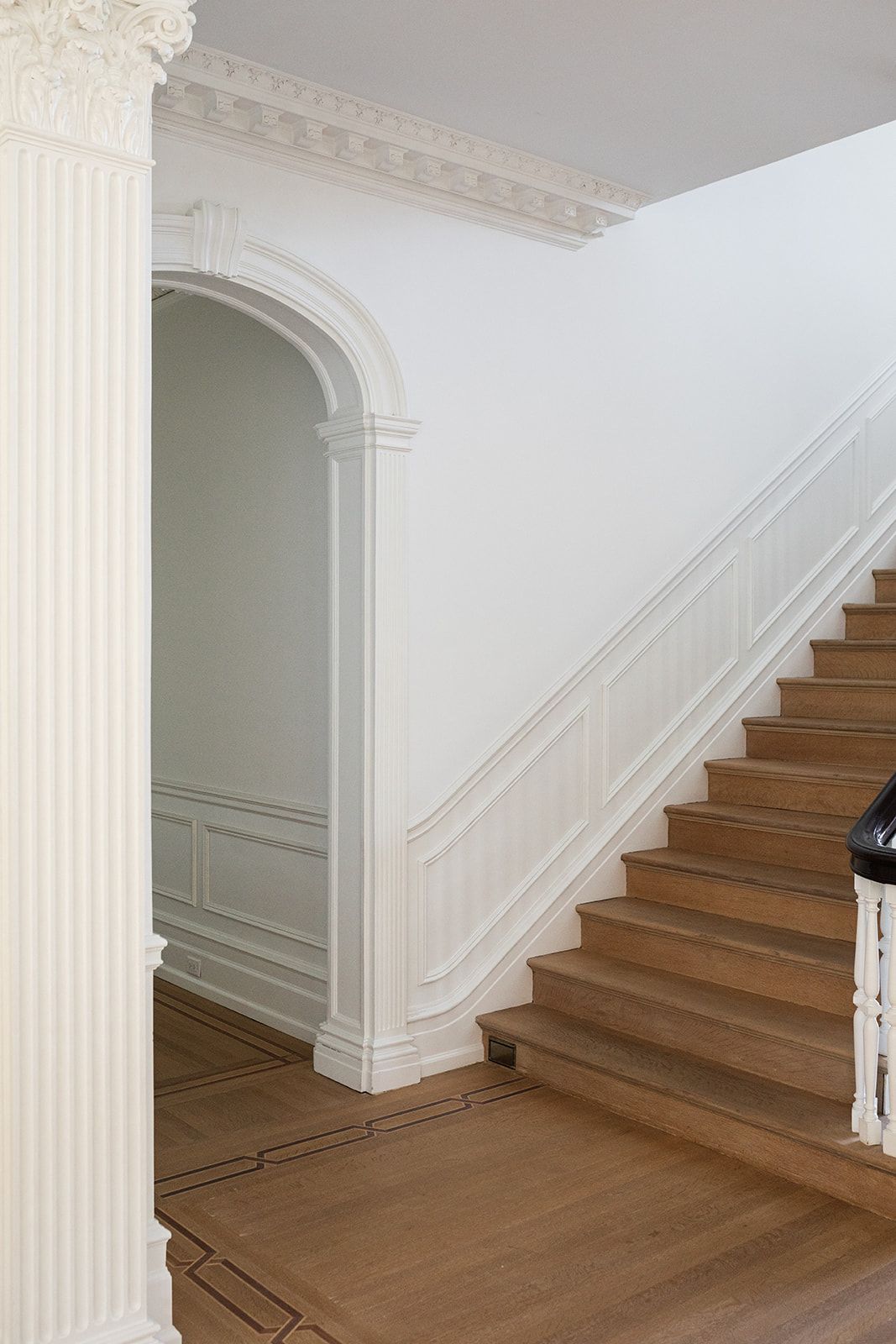 Classical white staircase with fluted column and detailed millwork showcases wooden treads.