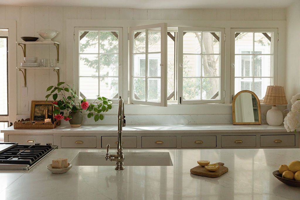 Bright white kitchen interior with vintage arched windows, quartz countertops, and modern stainless steel sink fixture.