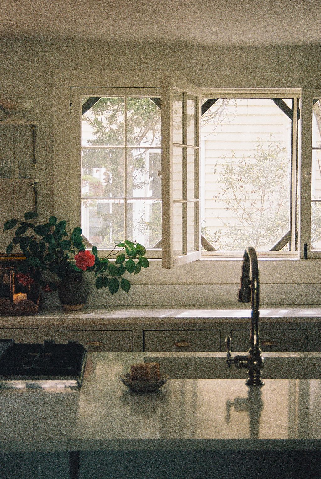 Sunlit kitchen counter with windows and potted plants, featuring a modern black faucet and sink in warm color tones.