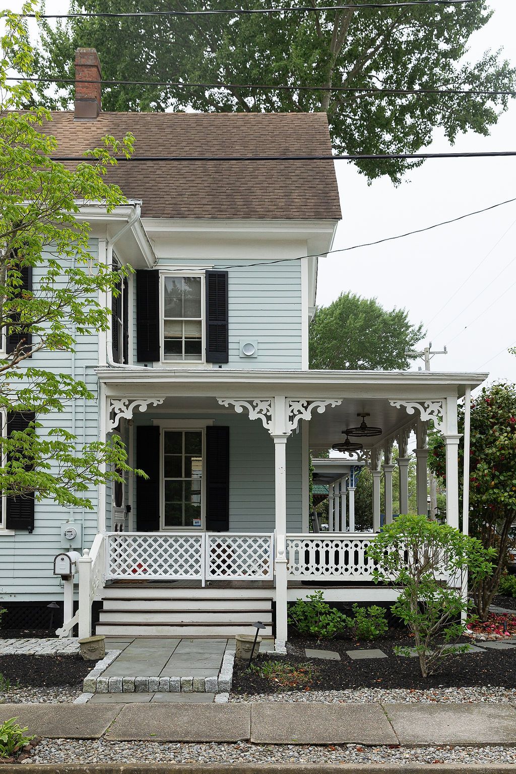 White Victorian style house with ornate wraparound front porch featuring decorative lattice and gingerbread trim details.