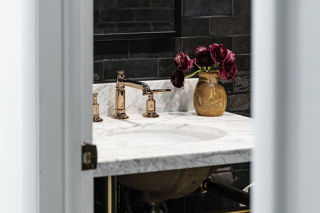 Elegant bathroom features marble countertops and dark wood cabinets with modern gold hardware and wall sconces.