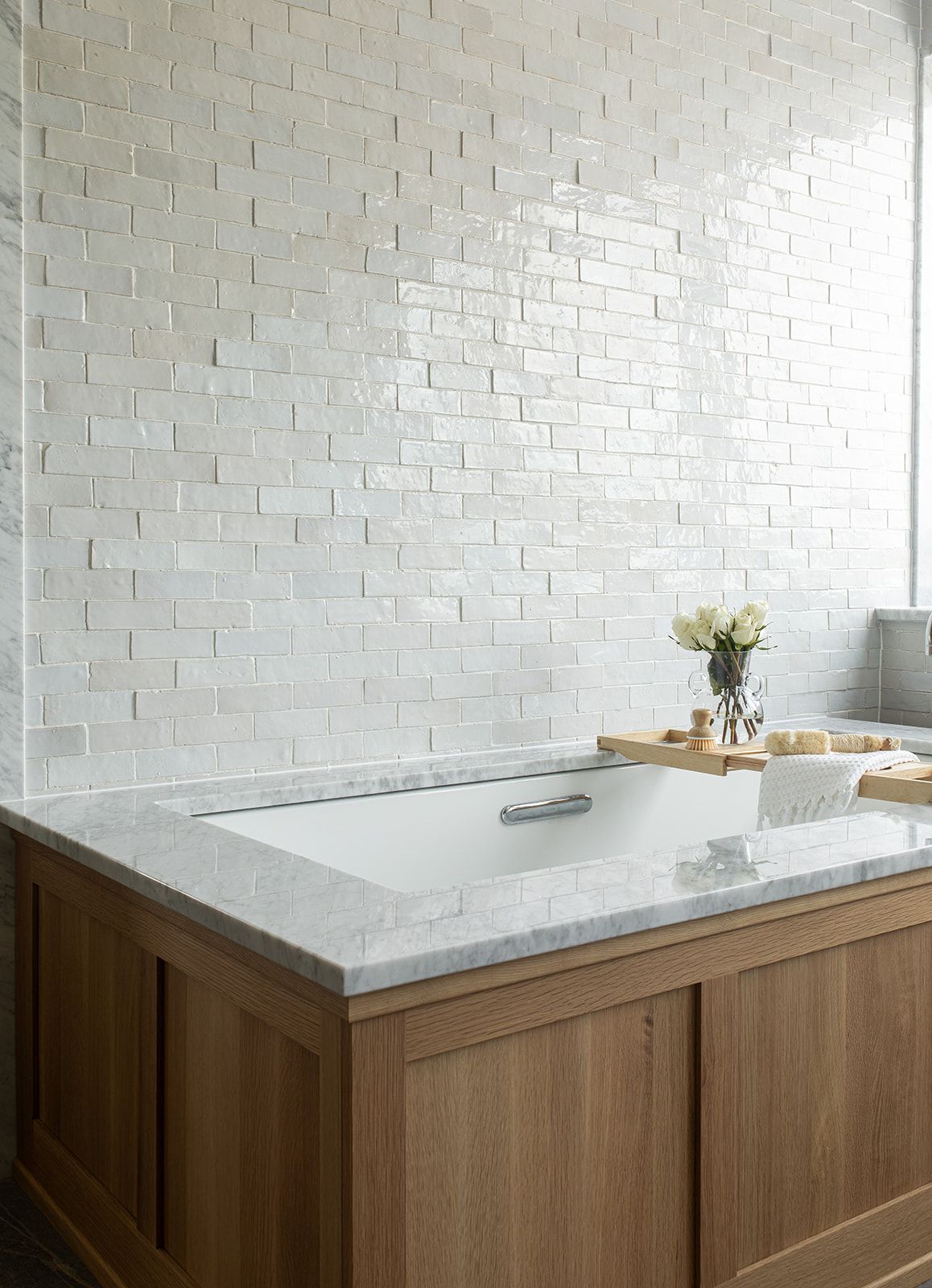 Elegant bathroom featuring a built-in soaking tub with marble surround, warm oak cabinetry, and white glazed brick wall tiles.