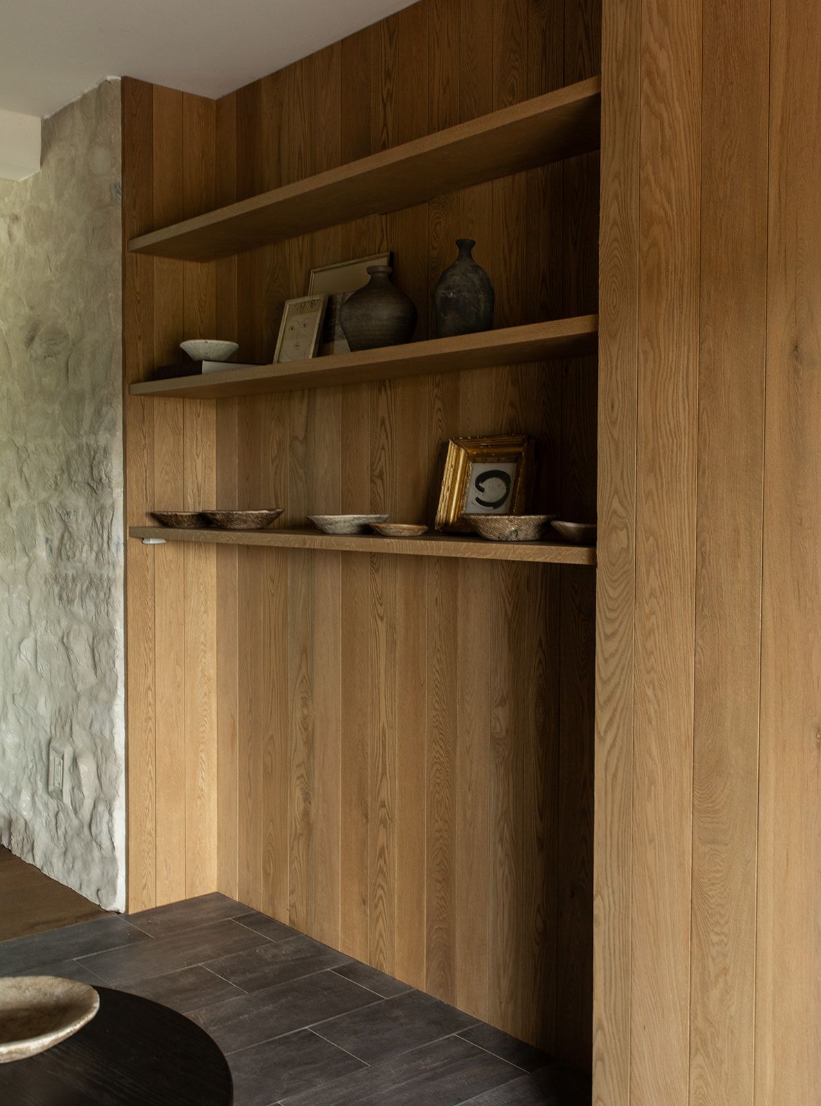 Built-in wooden shelving unit displaying ceramic vases, bowls, and decorative objects against a stone wall.