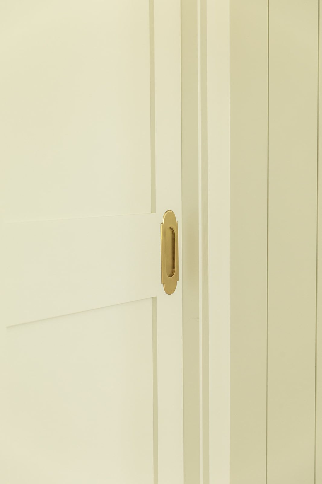Close-up of a white panel door with a recessed brass flush pull handle for a sliding door.