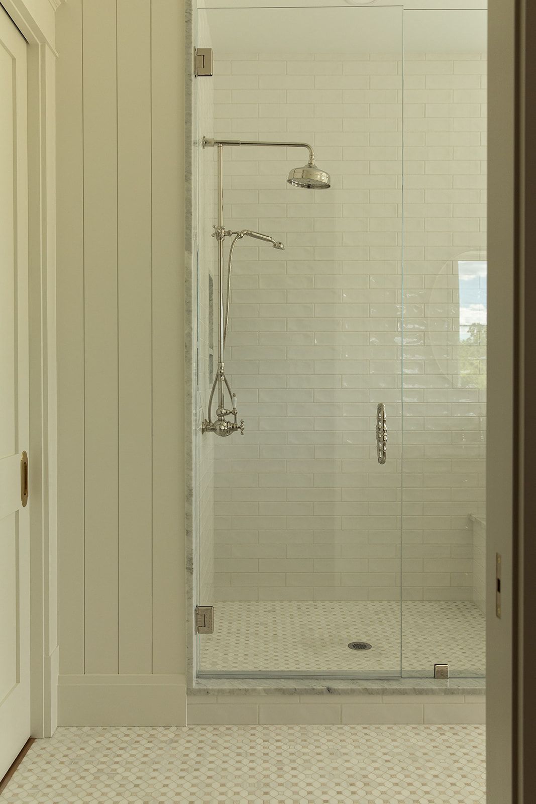 Glass walk-in shower with white subway tiles, mosaic floor, and polished chrome rainfall showerhead fixture.