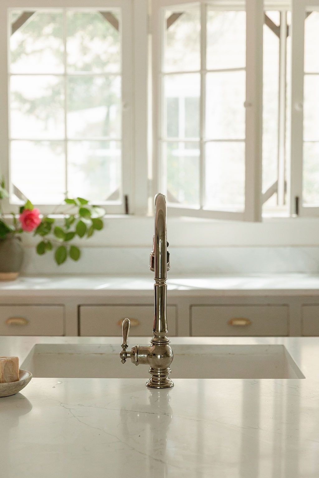 Modern brushed nickel faucet in bright white kitchen with large windows and marble countertops.