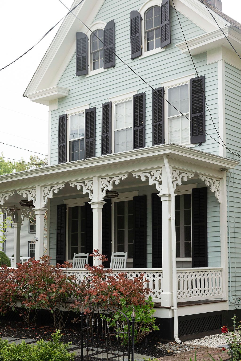 Historic Victorian home with mint green siding, black shutters, and ornate white porch featuring decorative gingerbread trim.