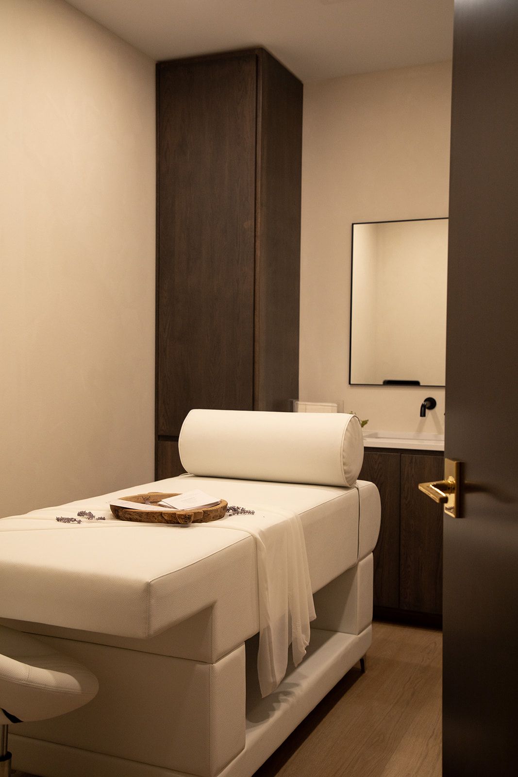 Serene spa treatment room with massage table, white linens, and dark wood accents.