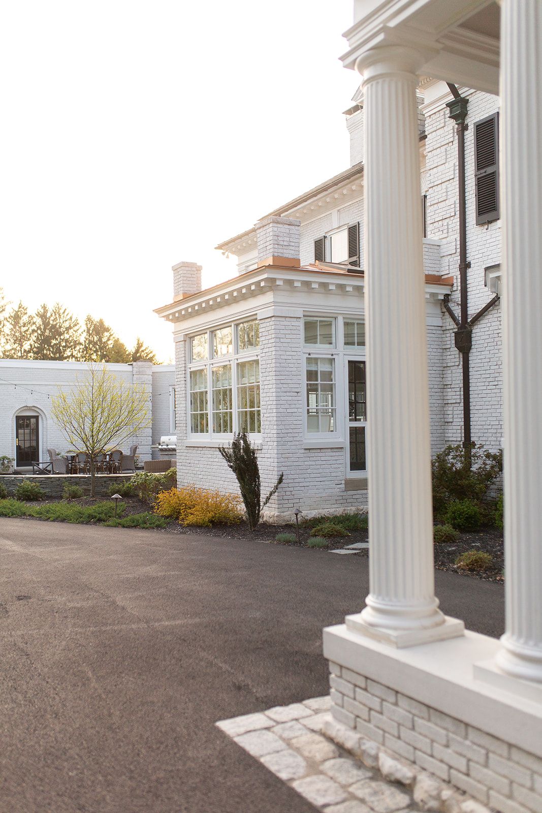 White colonial-style mansion with tall columns and bay windows viewed from the driveway.