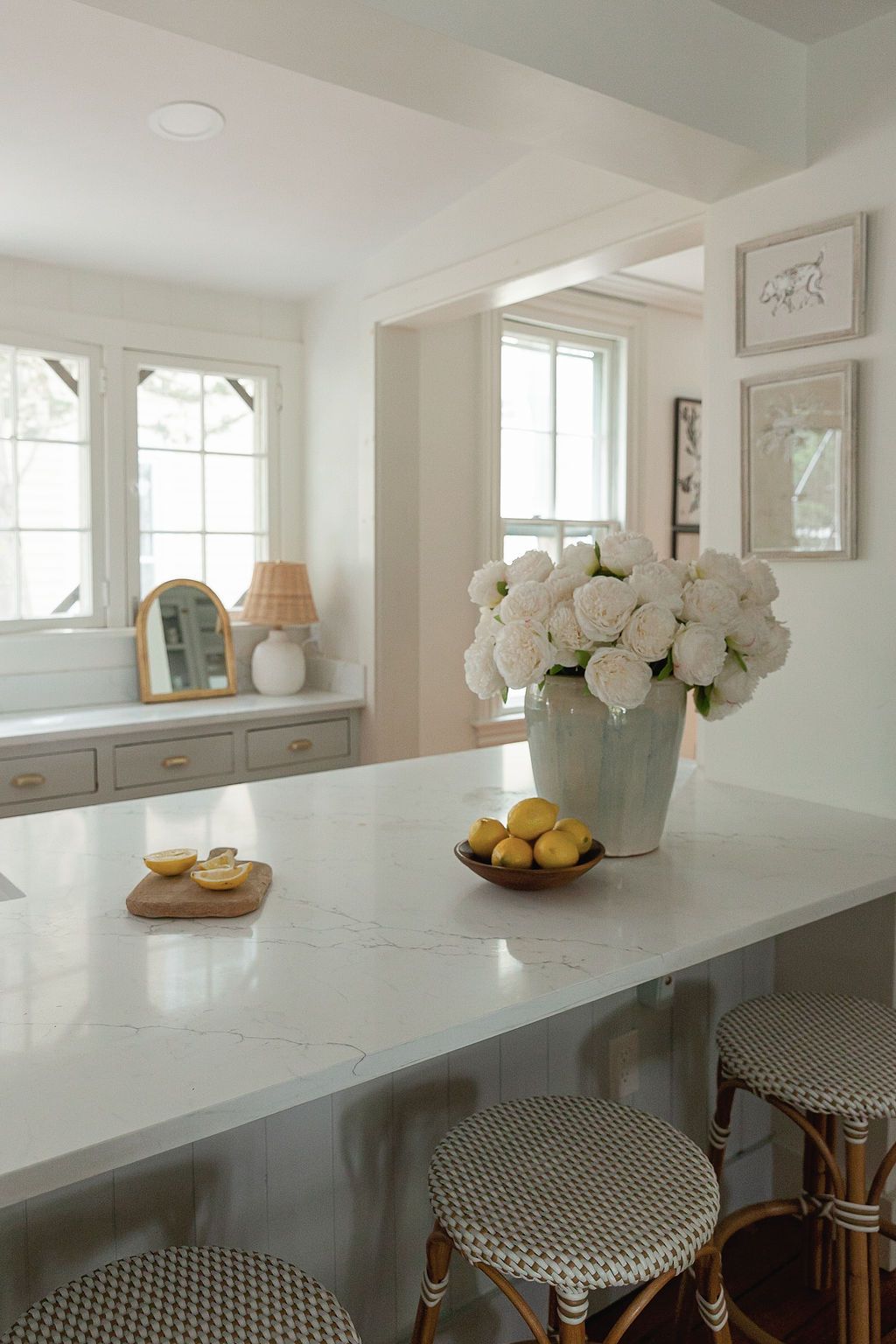 Modern white kitchen interior with marble countertop and black and white checkered bar stools next to a window.