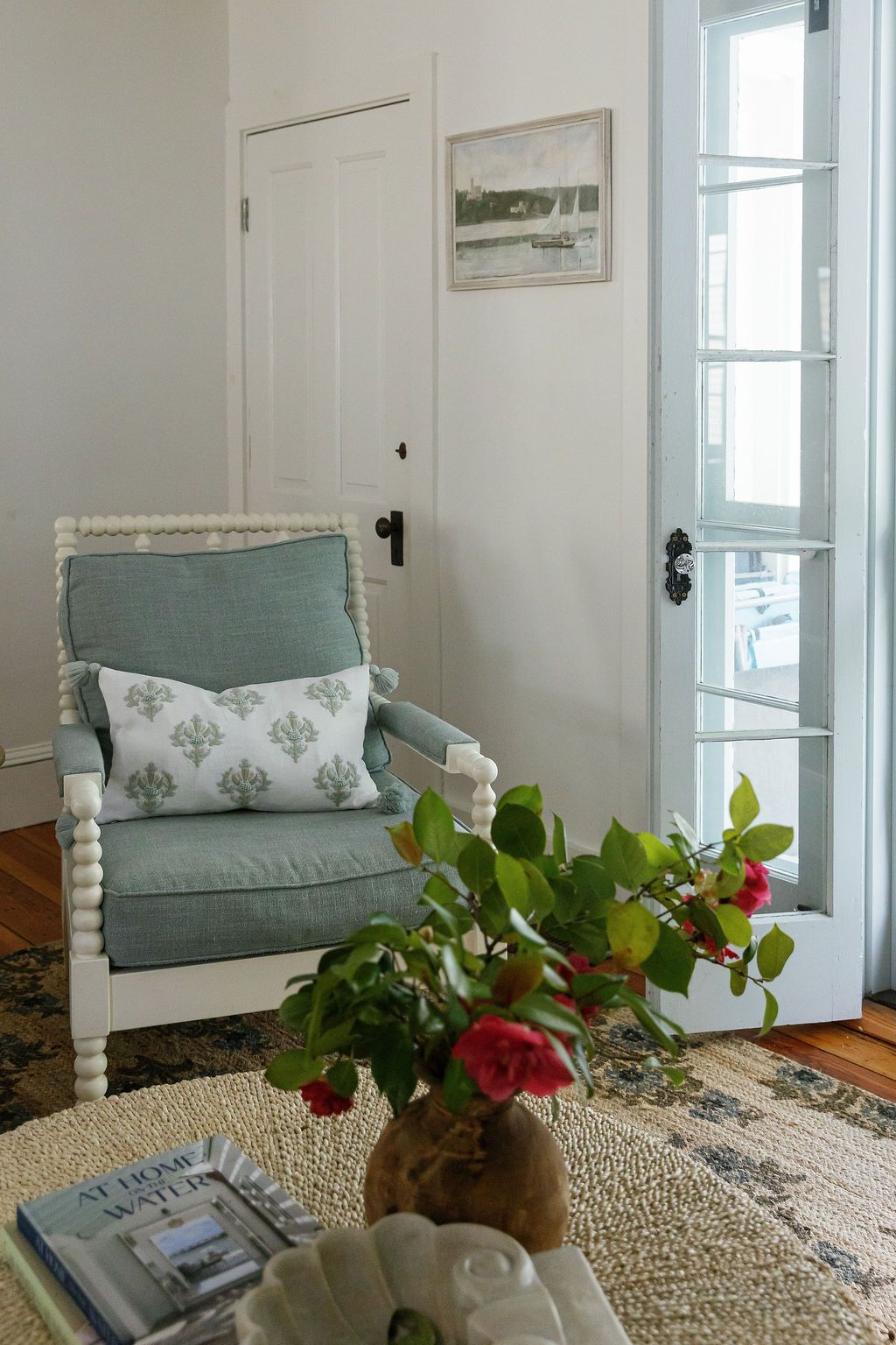 Coastal style entryway with natural jute rug, sage green cushions, and red roses in a rustic vase.