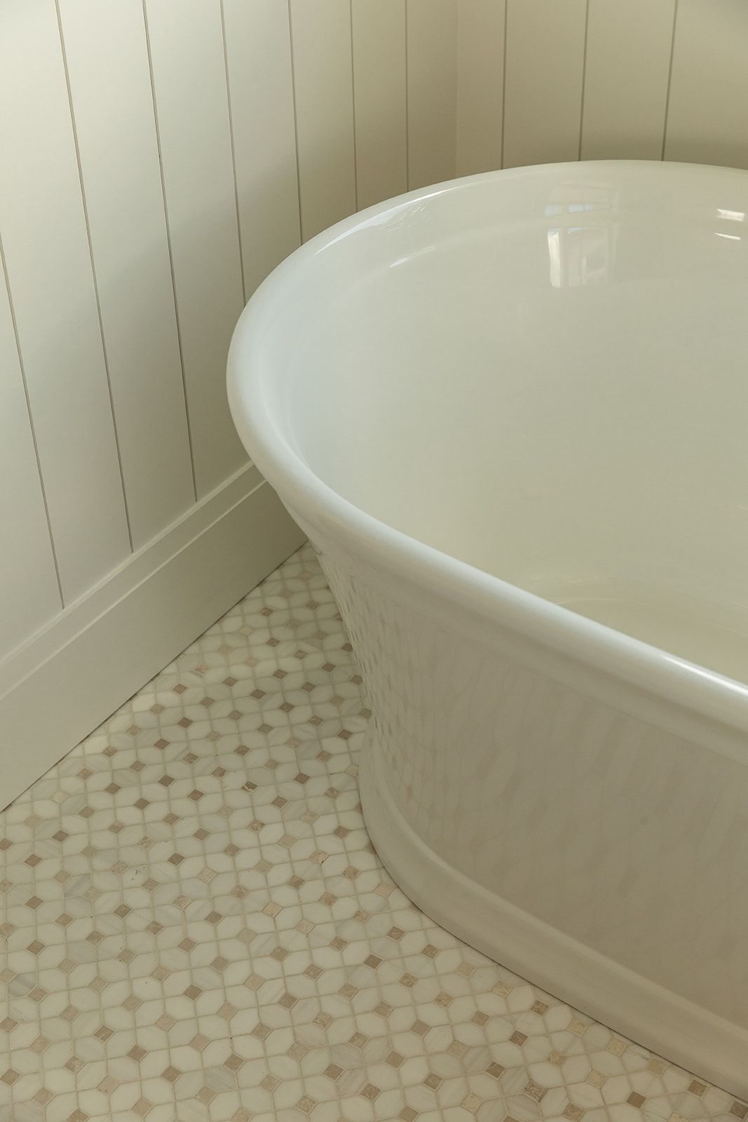 White freestanding bathtub in a bathroom corner with beadboard walls and classic mosaic tile flooring.