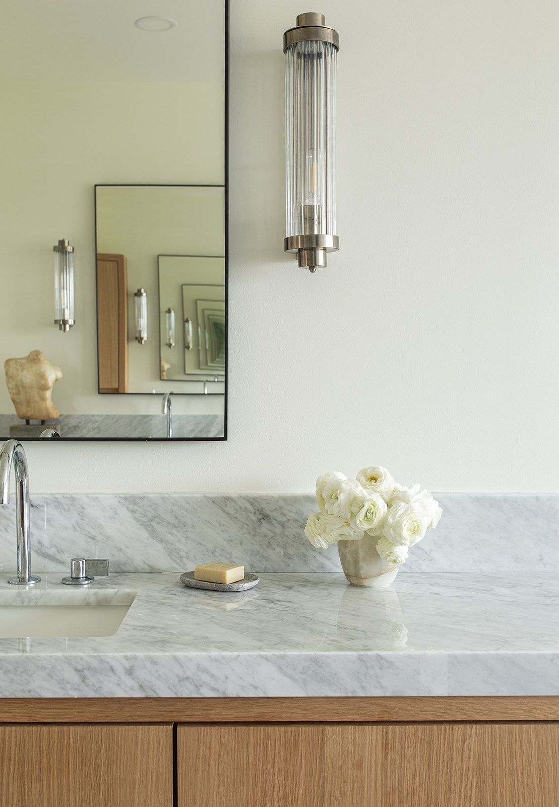 Marble bathroom countertop with undermount sink, crystal sconce, black mirror, and white rose arrangement.
