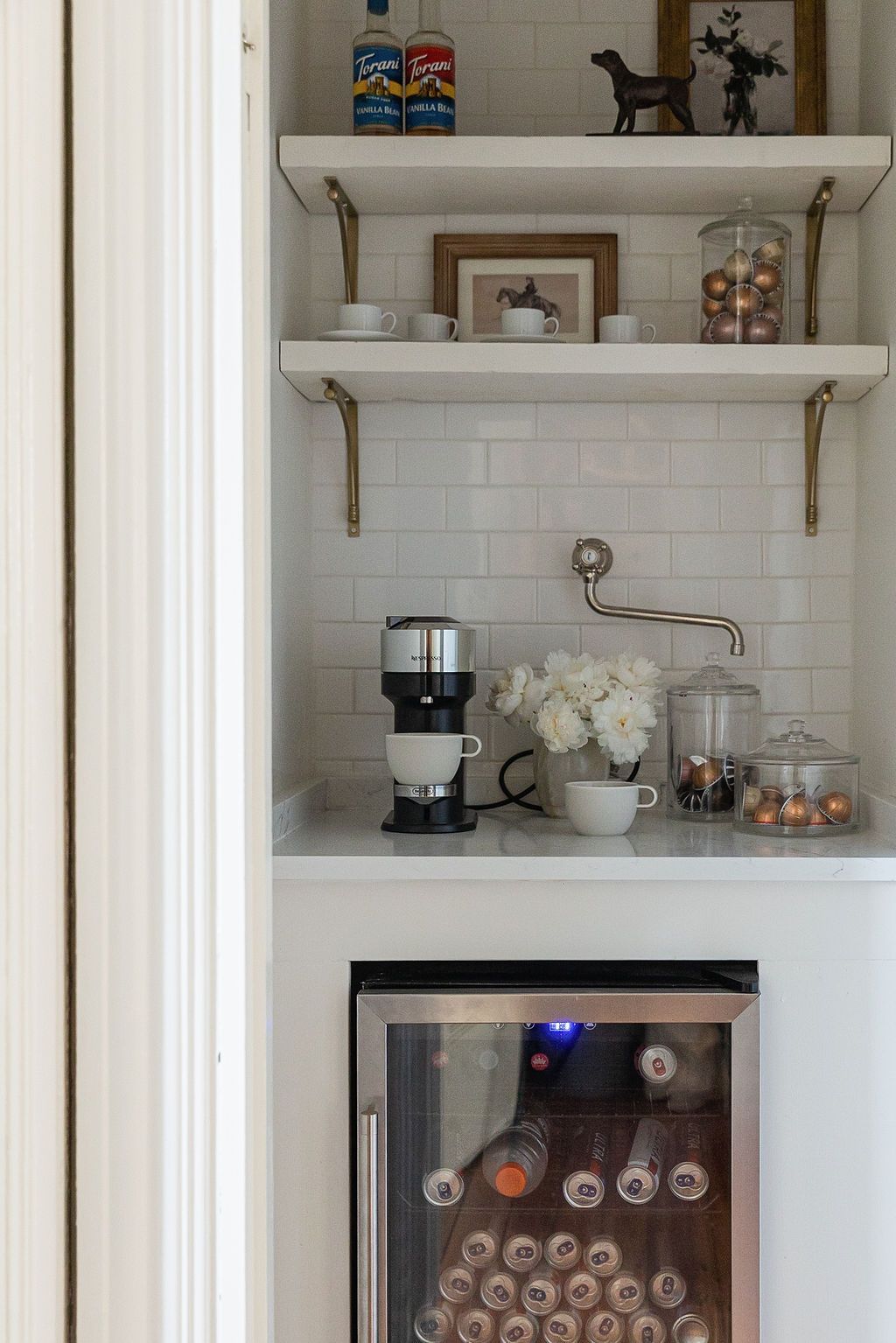 A stylish coffee station with white subway tile backsplash features floating shelves, a coffee maker, and beverage fridge below.
