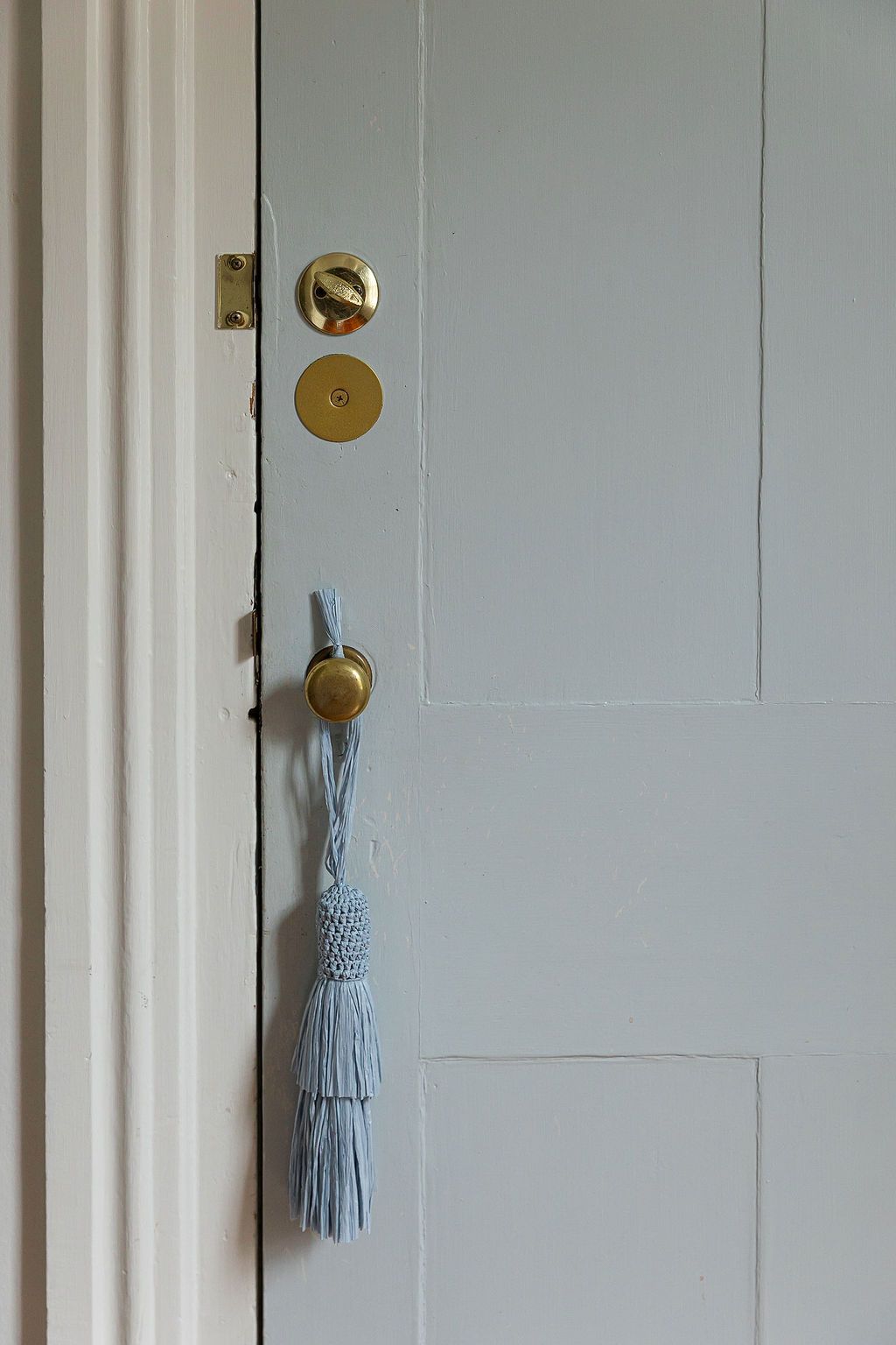 Three light blue tassels hang from brass doorknobs on white paneled doors in an interior hallway.