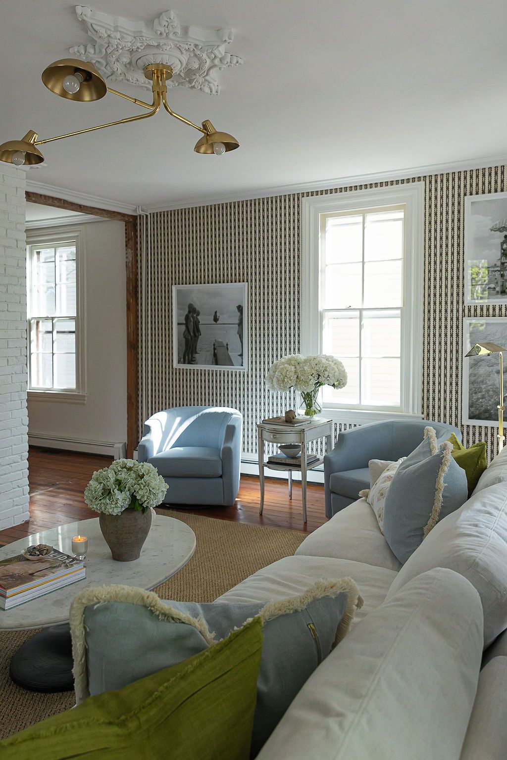 Modern living room interior with white walls, wooden slat dividers, comfortable upholstered seating, and brass light fixtures.