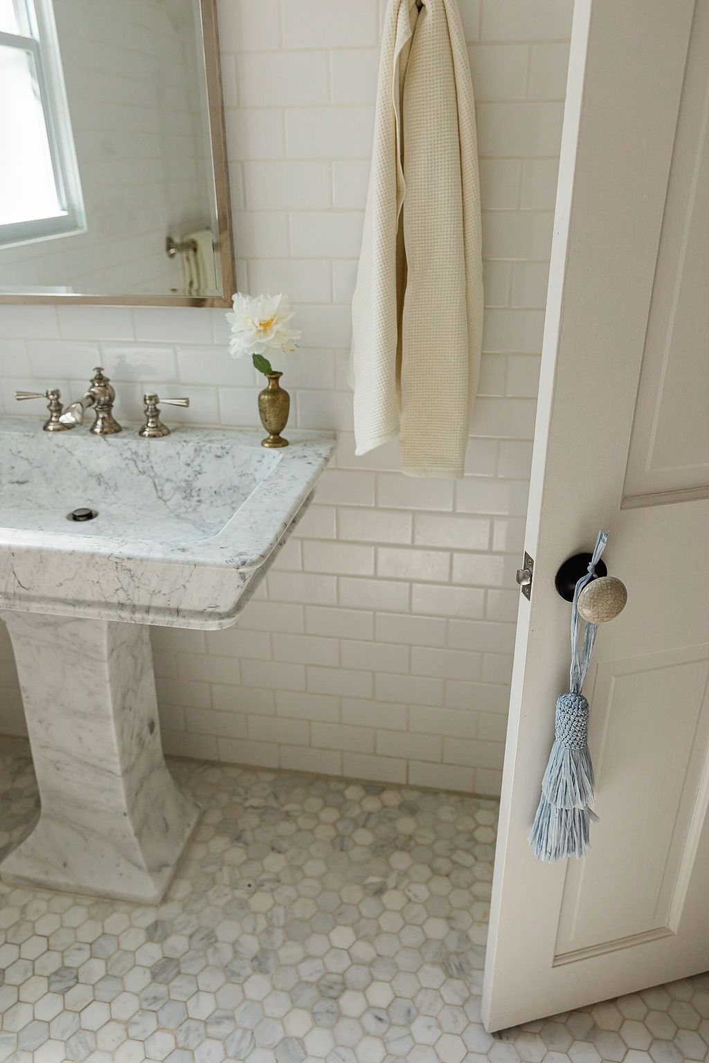 White marble bathroom features hexagonal floor tiles, subway wall tiles, and elegant pedestal sink with chrome fixtures.
