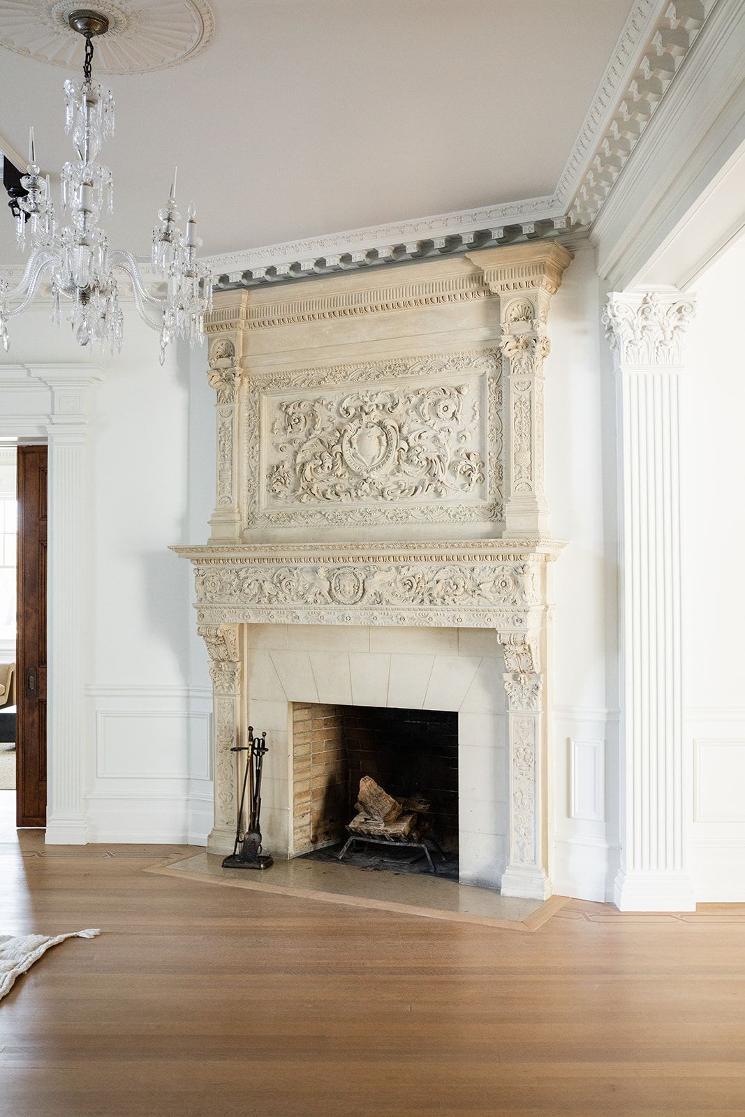 Ornate white marble fireplace with elaborate carved details and crystal chandelier in formal living room.