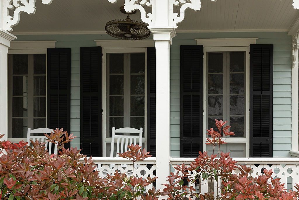 White columned porch with decorative trim and black shutters stretches across a classic home exterior.