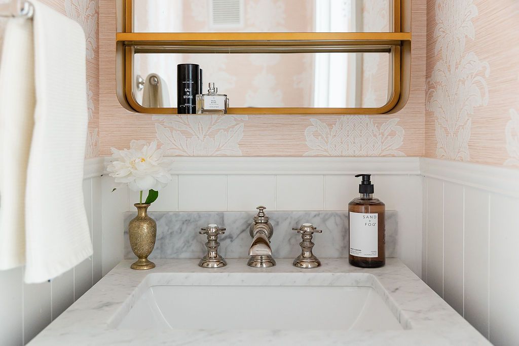 Elegant marble bathroom vanity with vintage silver faucets, glass soap dispenser, and gold-framed mirror above.