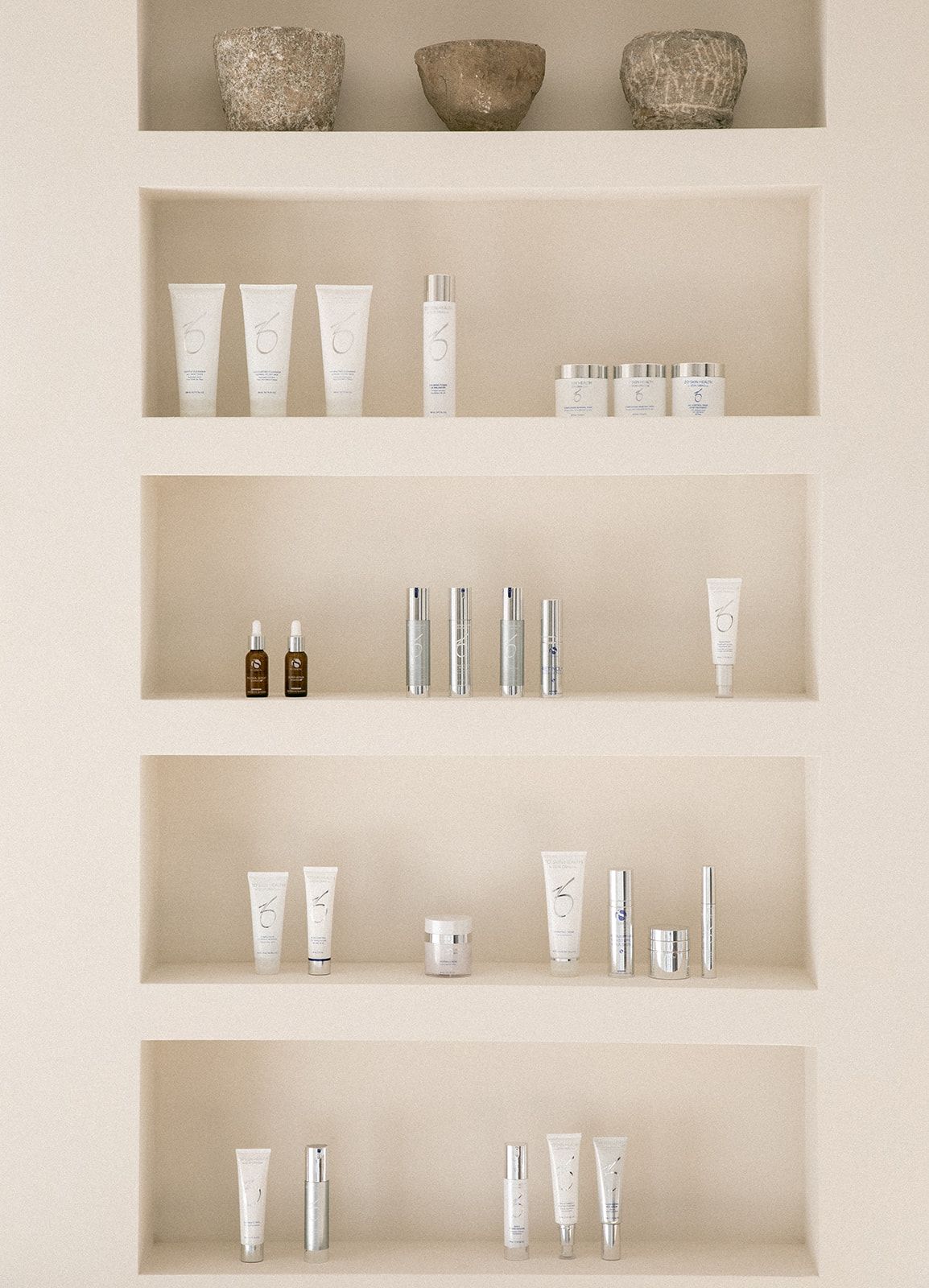 Minimalist white shelving unit displaying various skincare and beauty products in clean, organized rows.