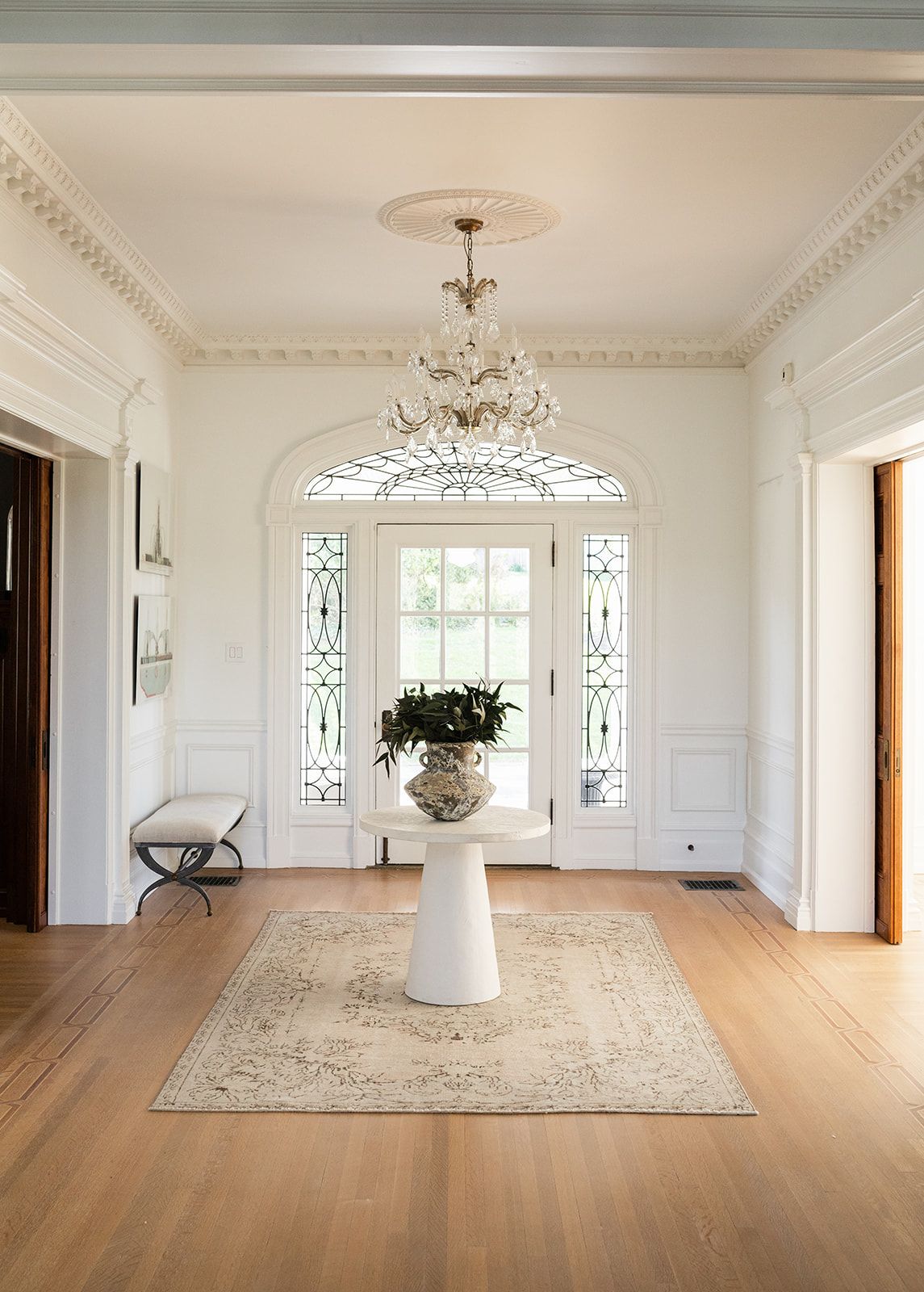 Elegant foyer with crystal chandelier, arched transom window, and pedestal table on patterned area rug.