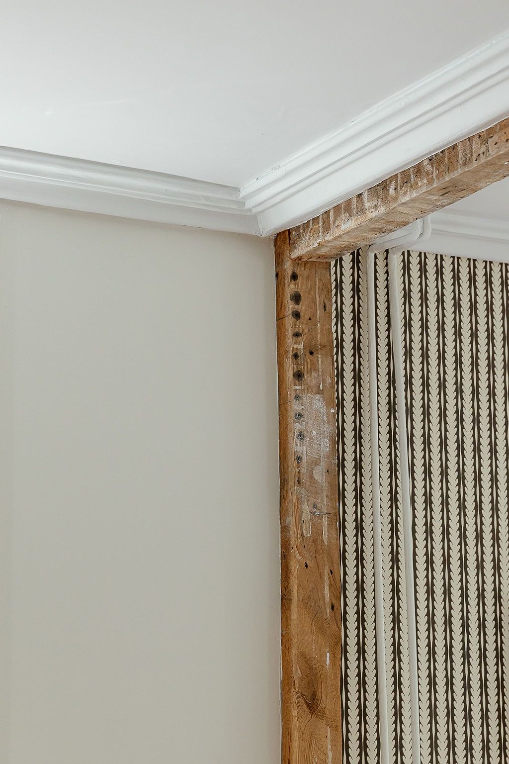 Rustic wooden door frame with decorative nails contrasts against white crown molding and striped curtain detail.