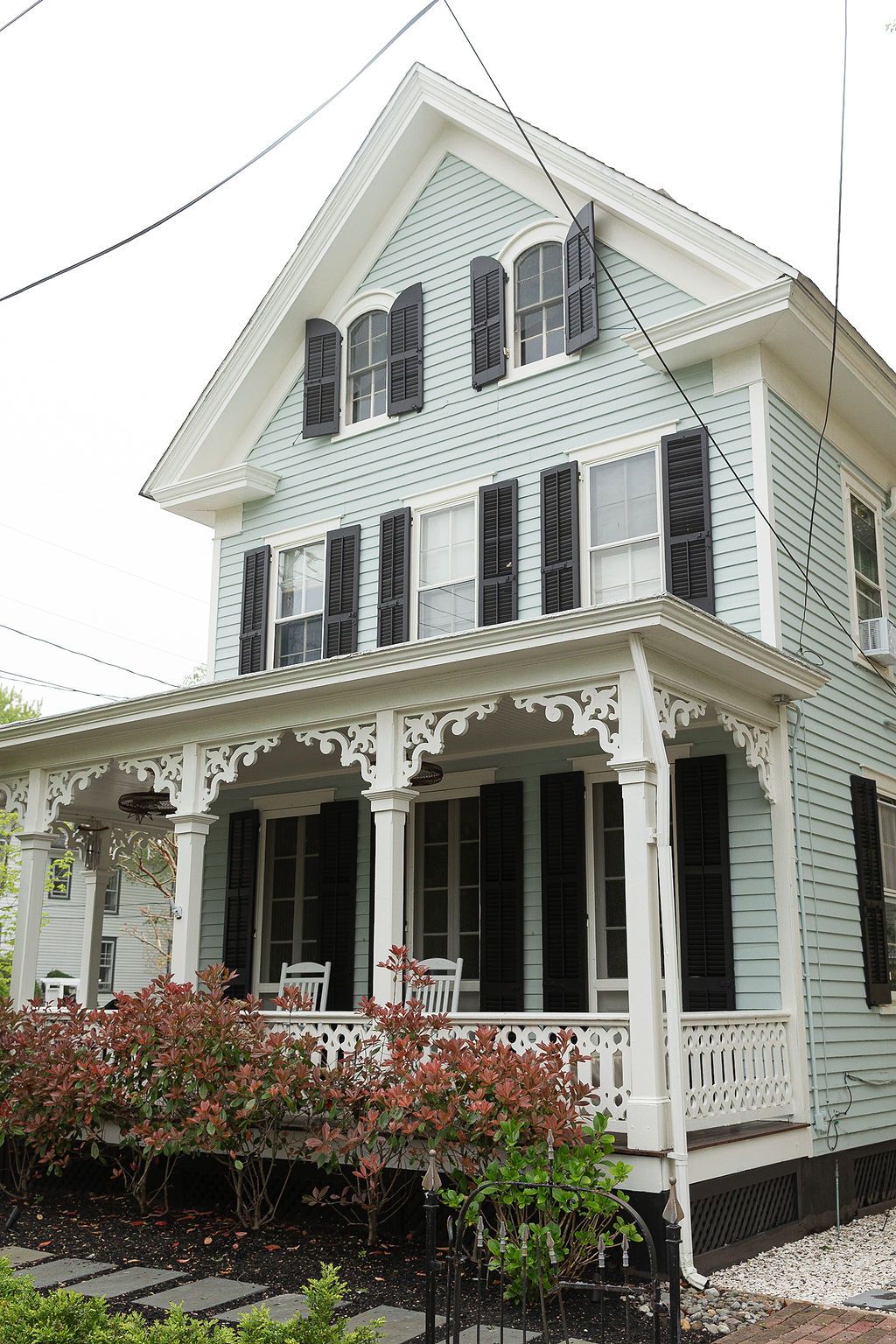 Elegant white Victorian house with black shutters and ornate wrap-around porch featuring decorative gingerbread trim details.