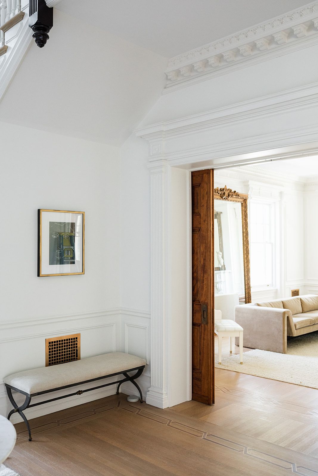Minimalist white hallway with wooden bench, framed artwork, and ornate crown molding.