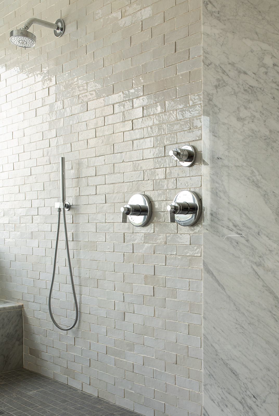 Elegant marble and white brick tile walk-in shower with chrome rain showerhead and dual control fixtures.