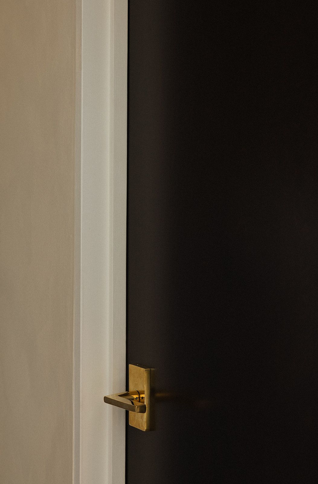 A modern brass door handle and lock mechanism mounted on a dark door with white trim.