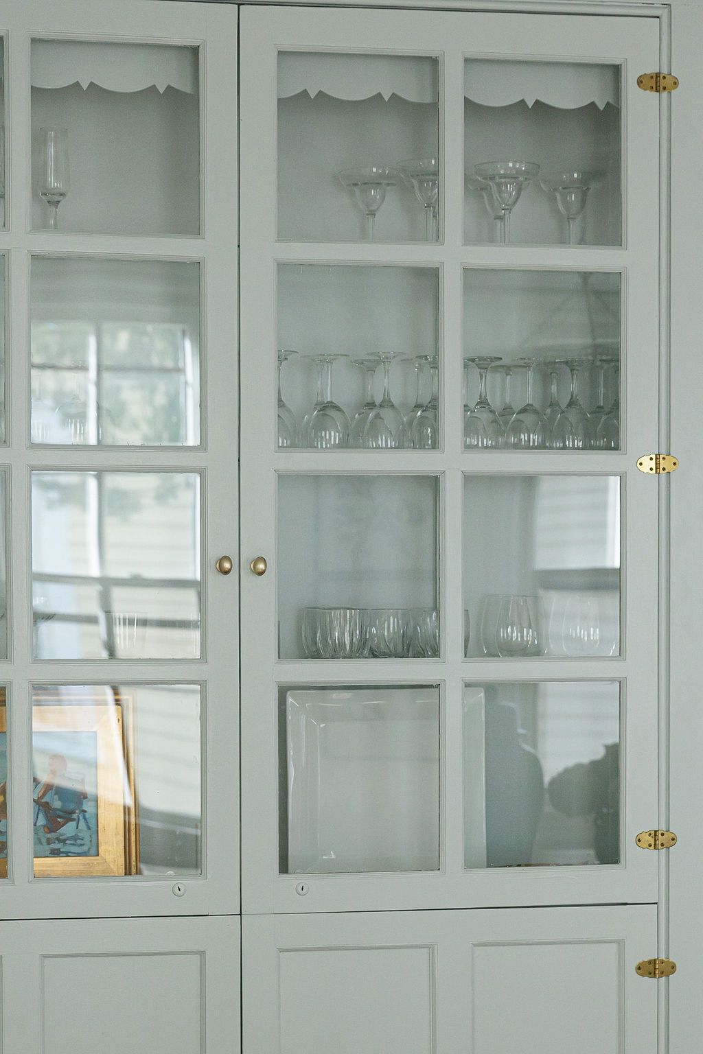 Vintage white glass cabinet displaying delicate glassware on multiple shelves with brass hardware and frosted glass doors.