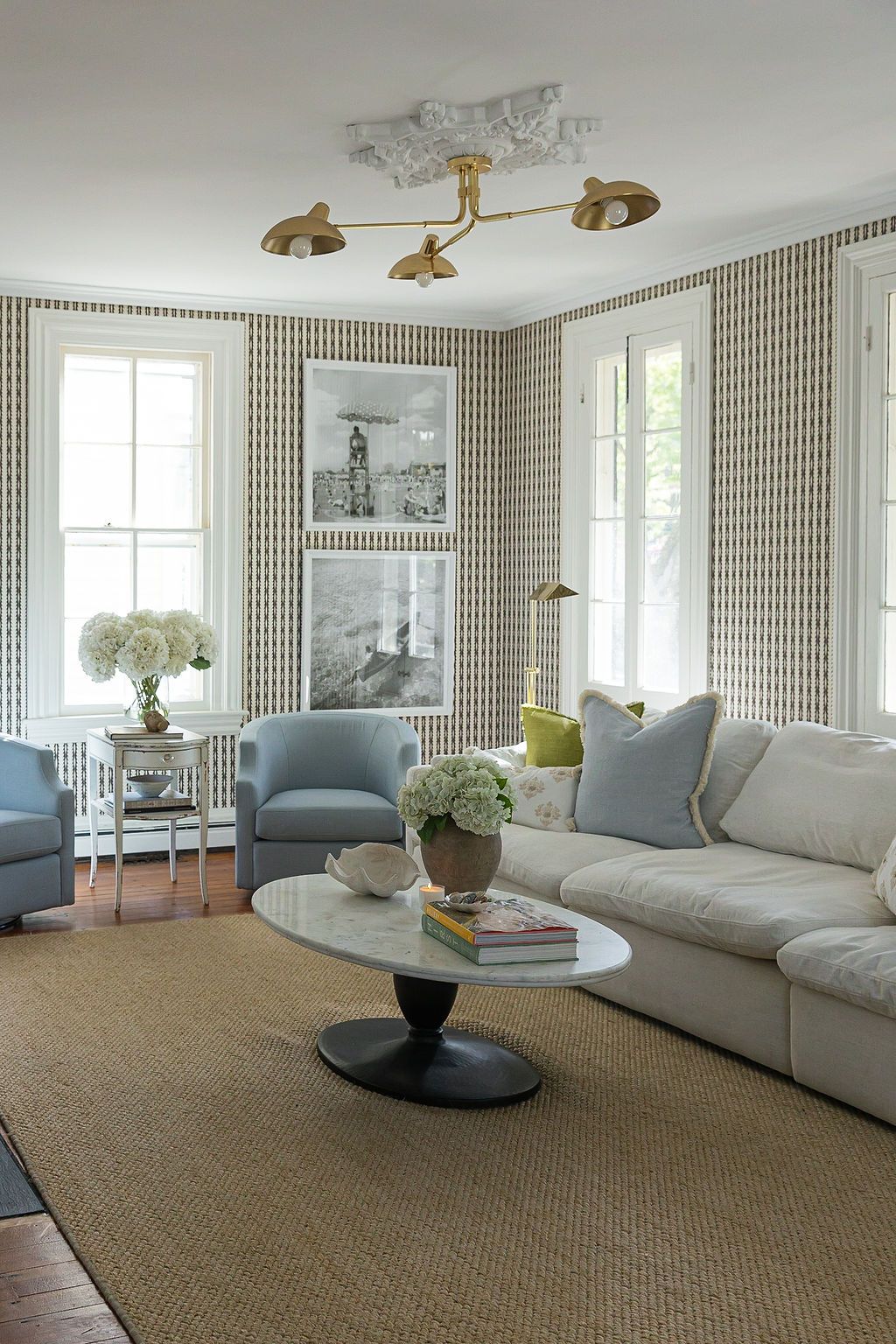 Modern coastal living room with sisal rug, white sofa, blue accent chairs, and brass lighting fixtures.