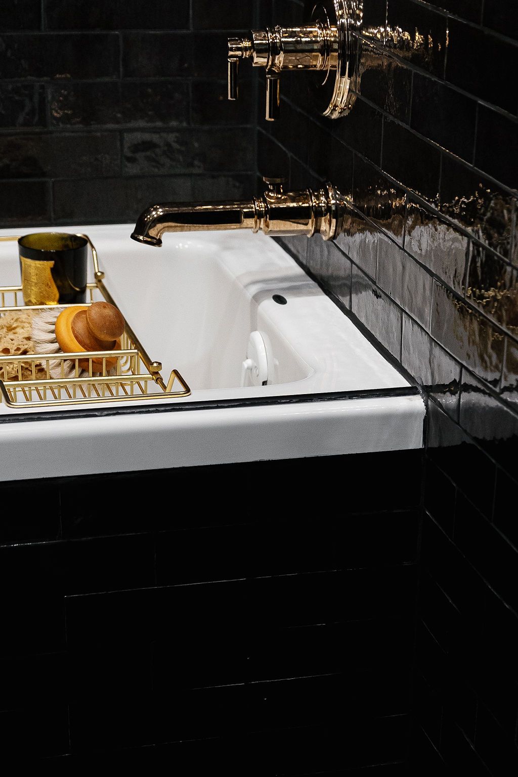 Luxurious white bathroom sink with gold faucet fixtures and drain tray against black tiled wall.