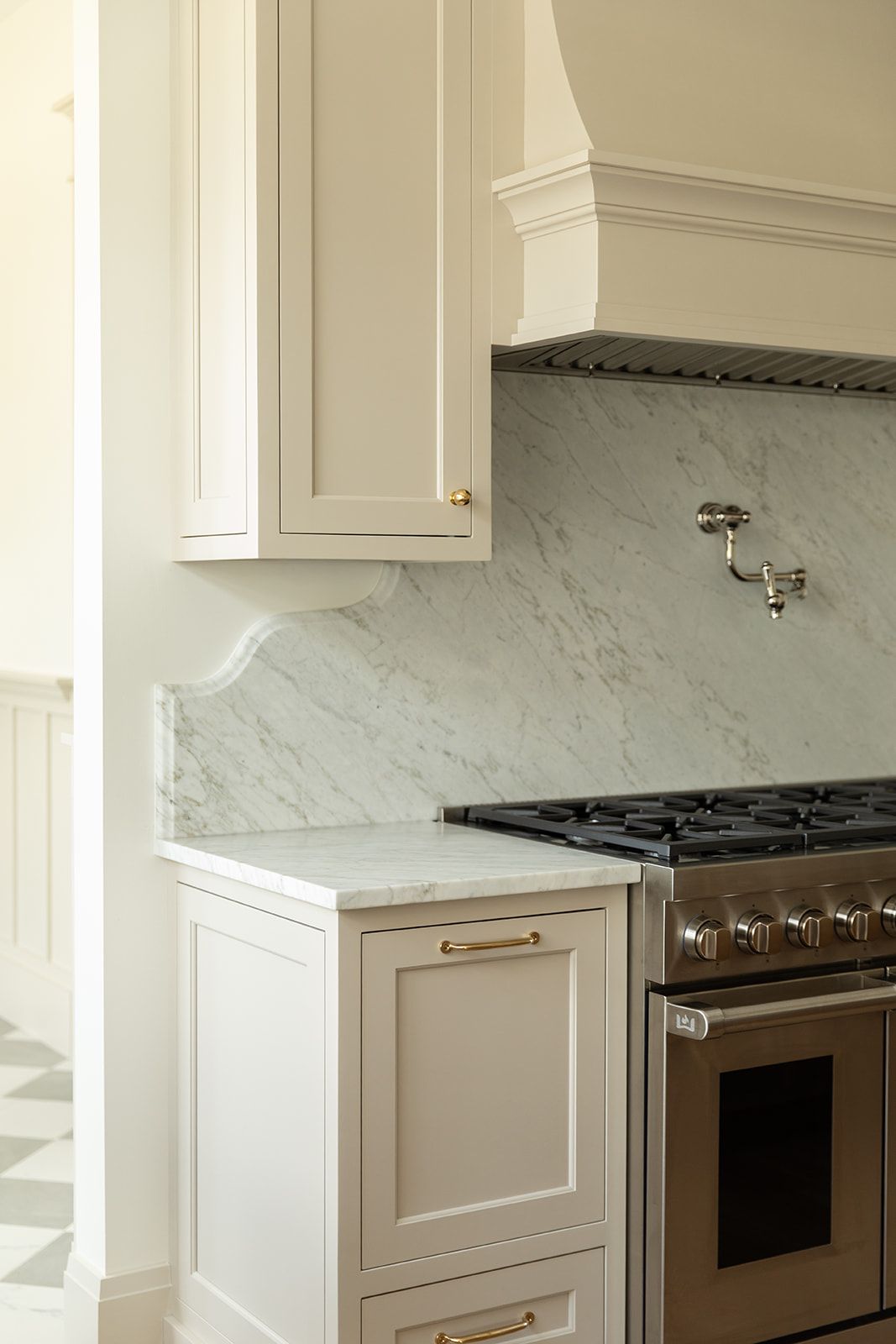 Elegant kitchen with marble backsplash, cream cabinets, brass hardware, and stainless steel range with custom hood.