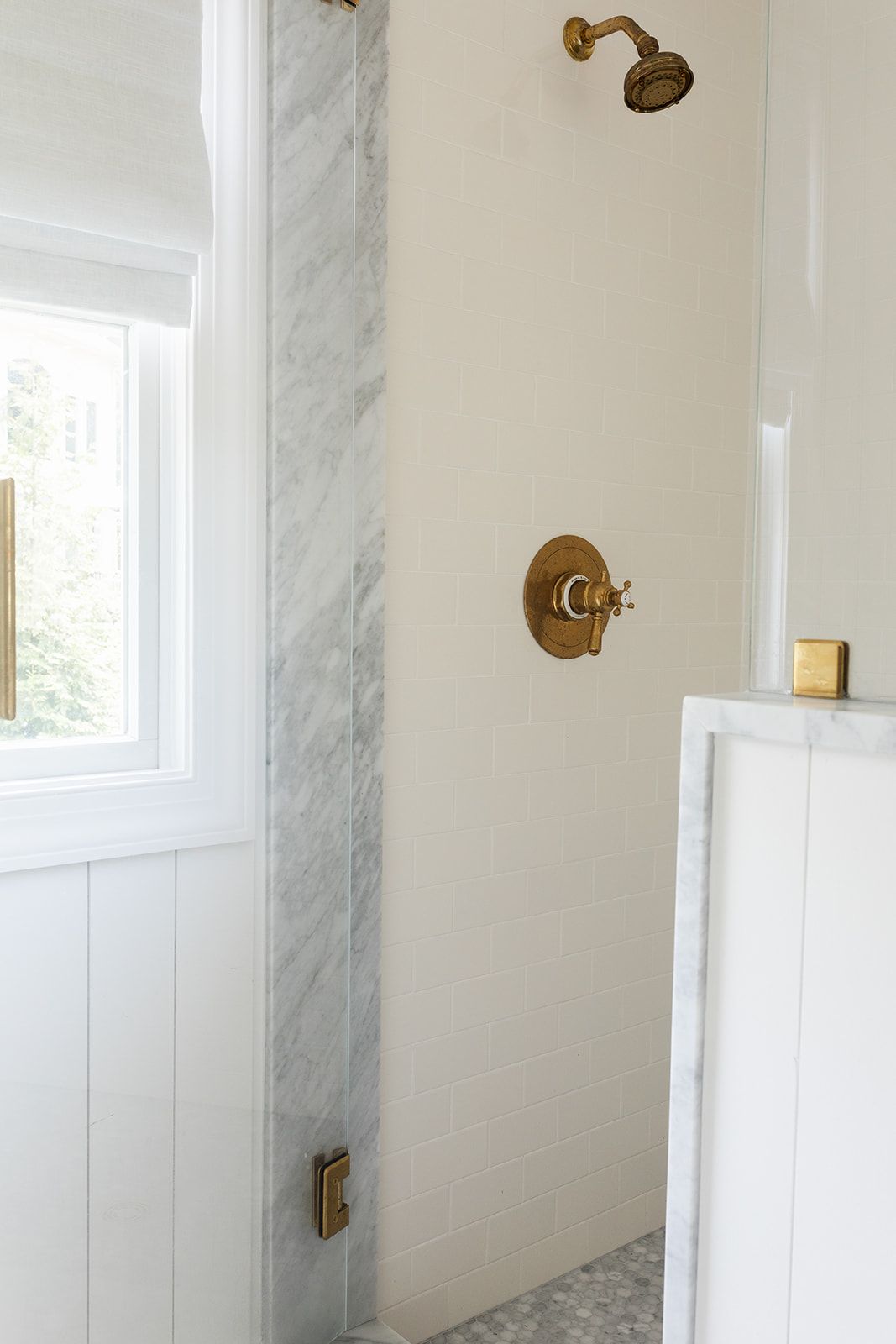 Elegant brass shower fixtures with marble surround and white subway tile in a bright bathroom.