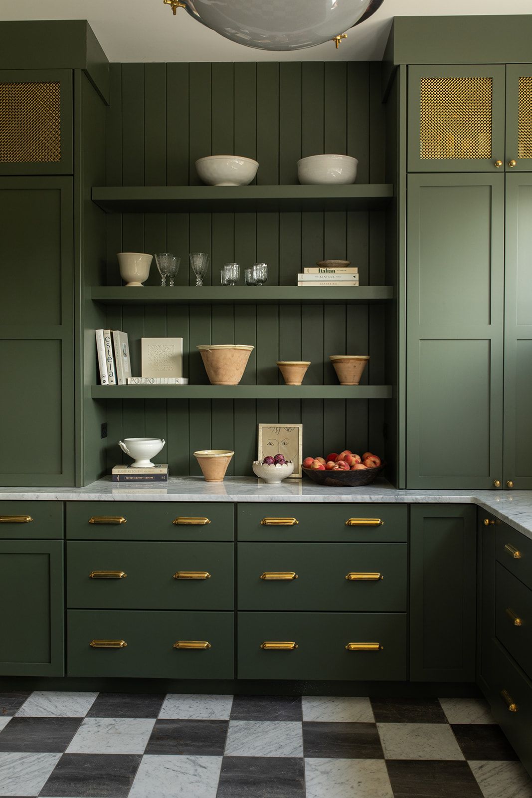 Dark green kitchen cabinets with gold hardware, open shelves, marble countertops, and black-and-white checkered floor.