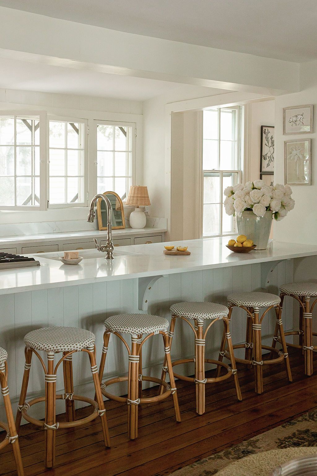 Rustic kitchen bar with row of elegant French bistro-style stools along white counter against hardwood floors and windows.