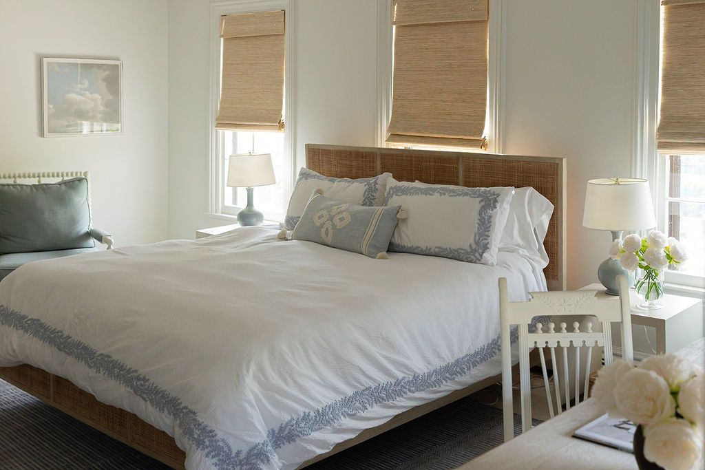 Serene bedroom with white linens, bamboo shades, and natural light creating a peaceful coastal ambiance.