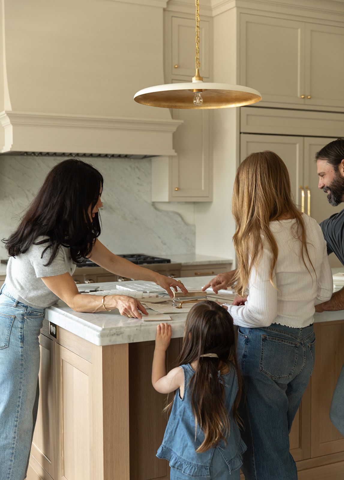 Family gathered around a kitchen island in a bright, modern kitchen with marble backsplash and gold pendant light.