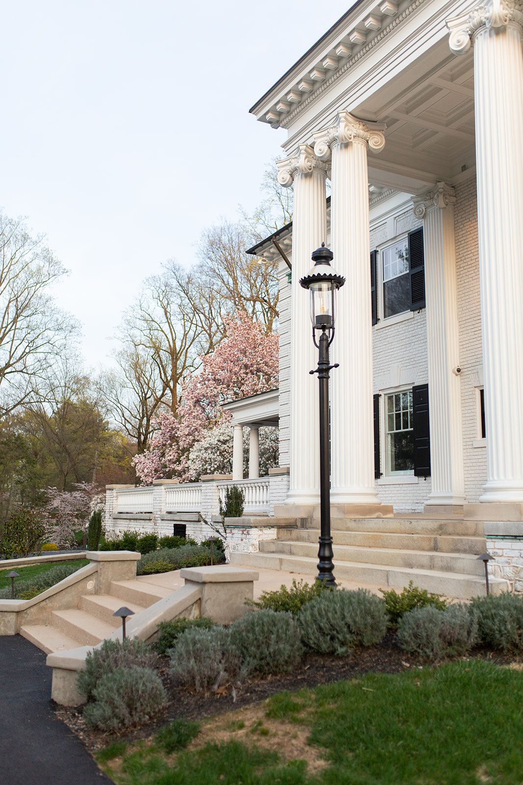 Historic mansion entrance with classical columns, vintage lamp post, and landscaped gardens.