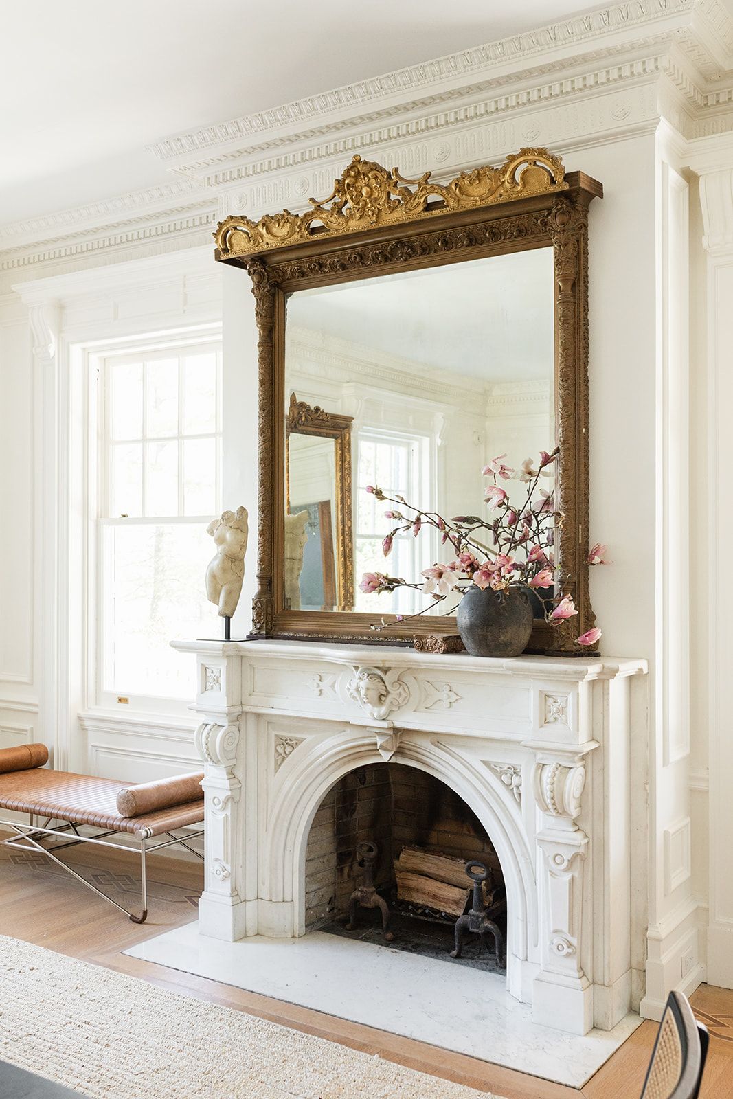 Classic white marble fireplace with decorative gold mirror and pink floral arrangement.