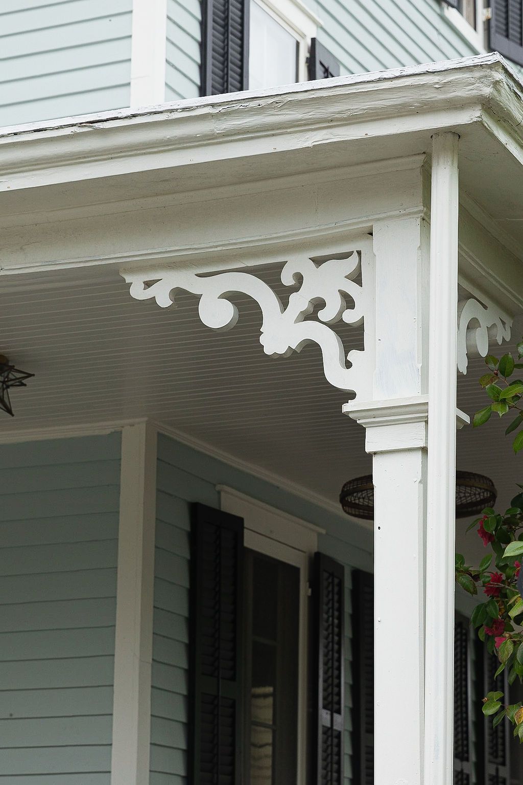 Ornate white Victorian porch detail showing decorative corbels and trim work against light blue siding.