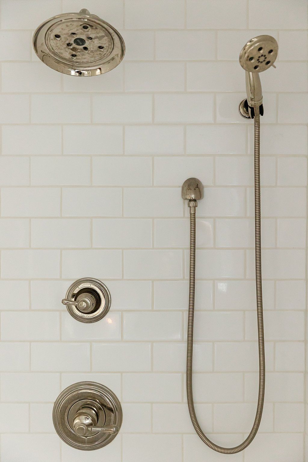 Modern bathroom shower head and handheld sprayer in brushed nickel finish mounted on white subway tile wall.