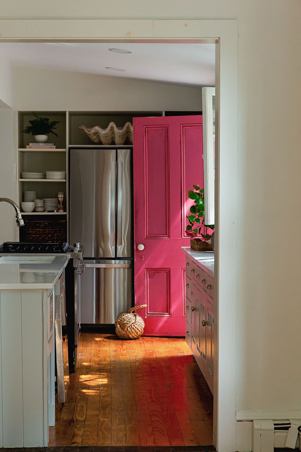 View through doorway into kitchen with bright pink interior door and stainless steel refrigerator on hardwood floors.