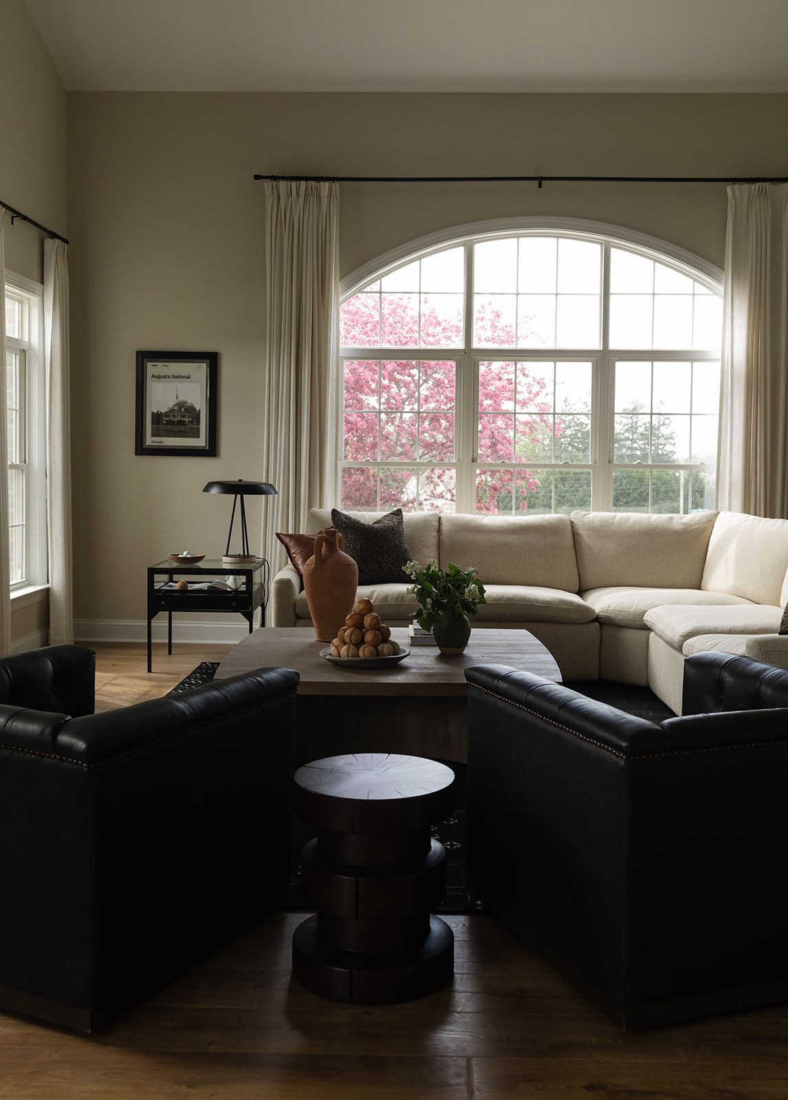 Modern living room interior features dark hardwood floors, arched windows, and natural light filtering through white curtains.