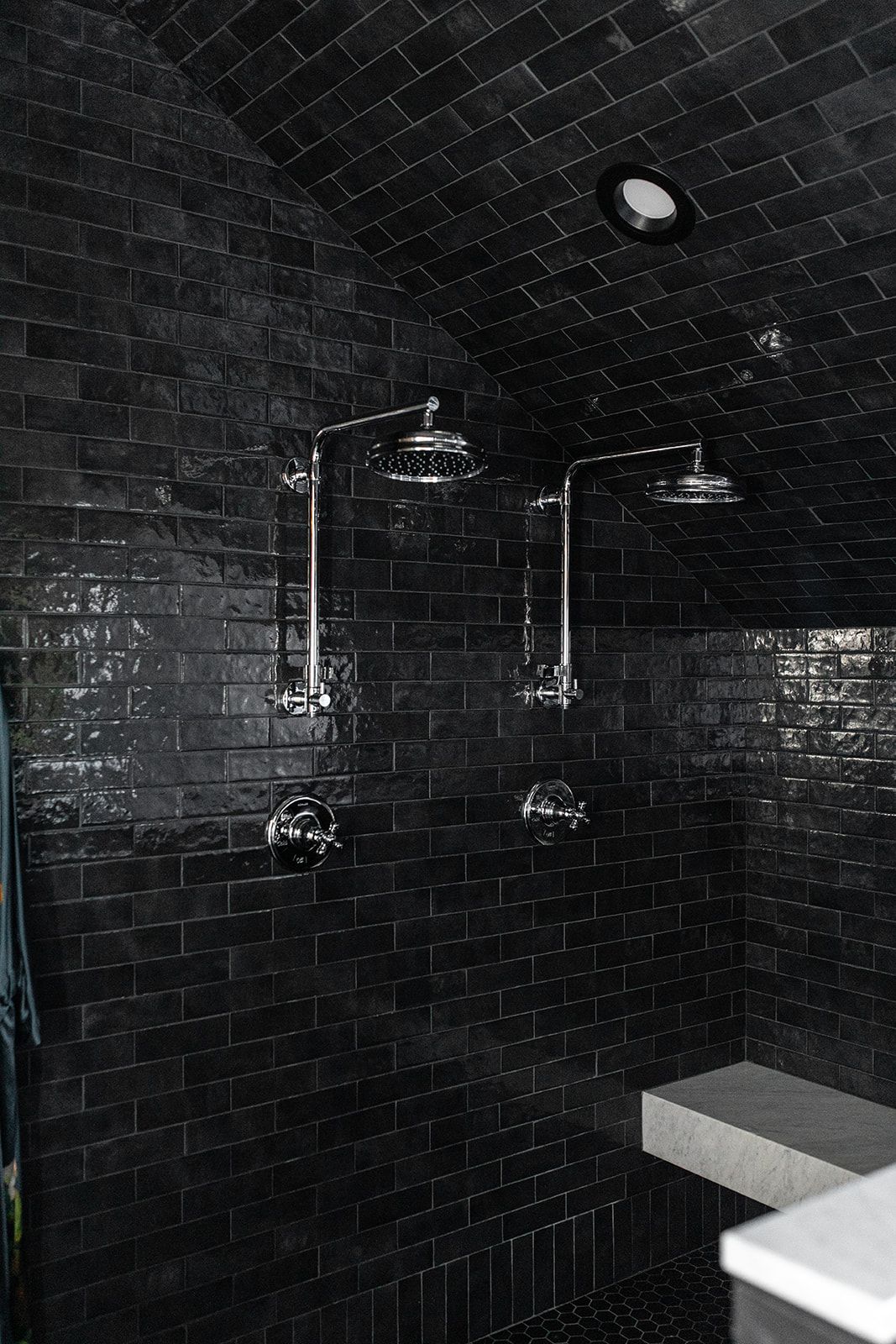 Modern shower room with glossy black subway tiles and dual rainfall showerheads.