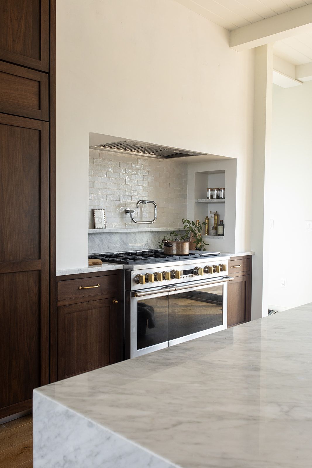 Luxury kitchen with dark walnut cabinets, marble island, and professional stainless steel range with tile backsplash.