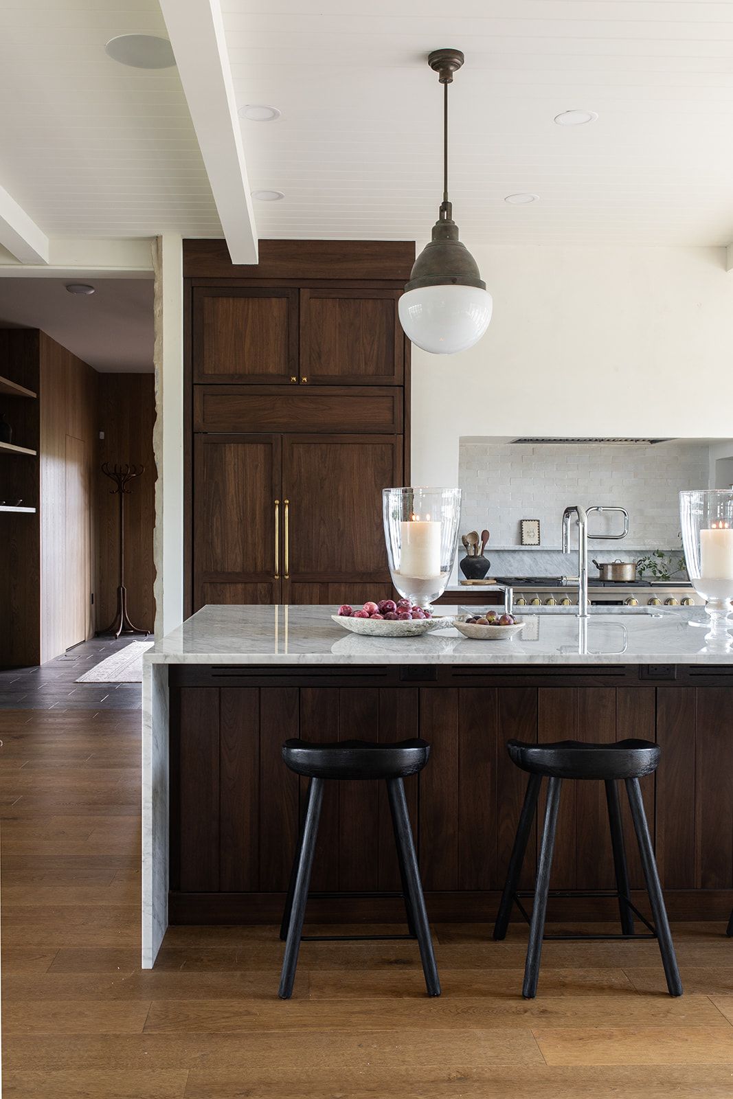 Dark walnut kitchen island with marble countertop, black bar stools, and pendant light in modern kitchen.